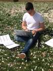 Male student sitting on grass with a laptop computer.